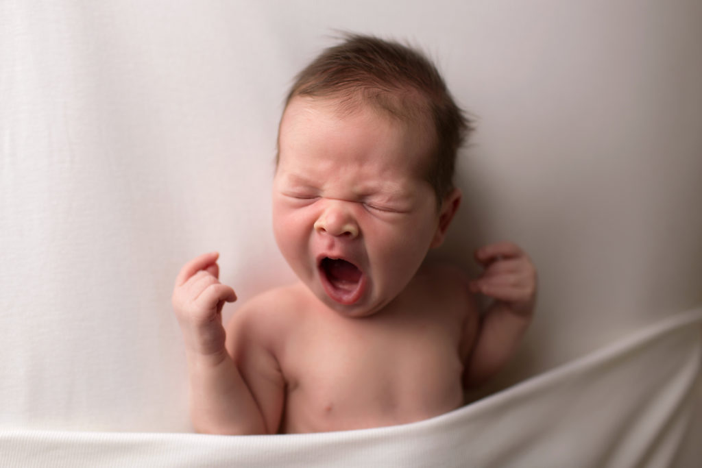 yawning newborn baby on a bedsheet